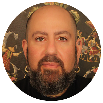Ahimsa Piercing Studio staff member Adam wearing yellow gold facial jewelry and yellow gold earrings standing in front of the studio's wallpaper