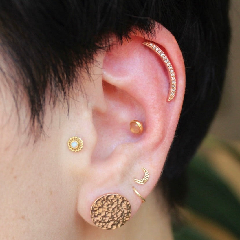 Left ear featuring an assortment of 14k Rose gold jewelry all from BVLA including a "Cumulus" in a helix with diamonds, a "Hammered Crescent Moon" a fitted "Seam Ring" and a "Hammered Solid Plug" in a stretched earlobe