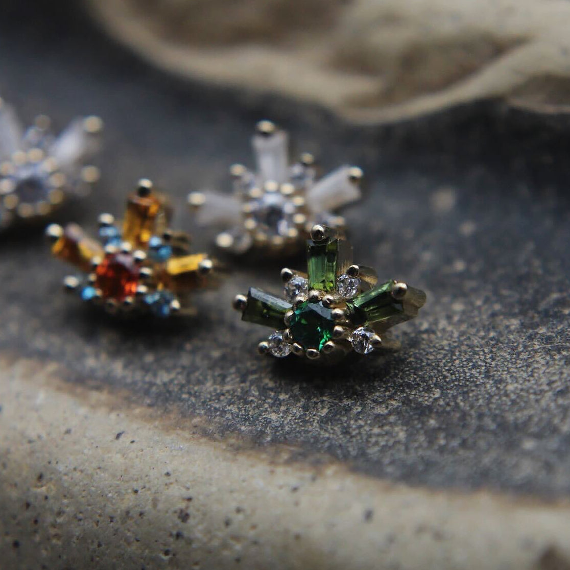 Close-up of decorative earrings on a textured surface featuring orange, green and clear stones