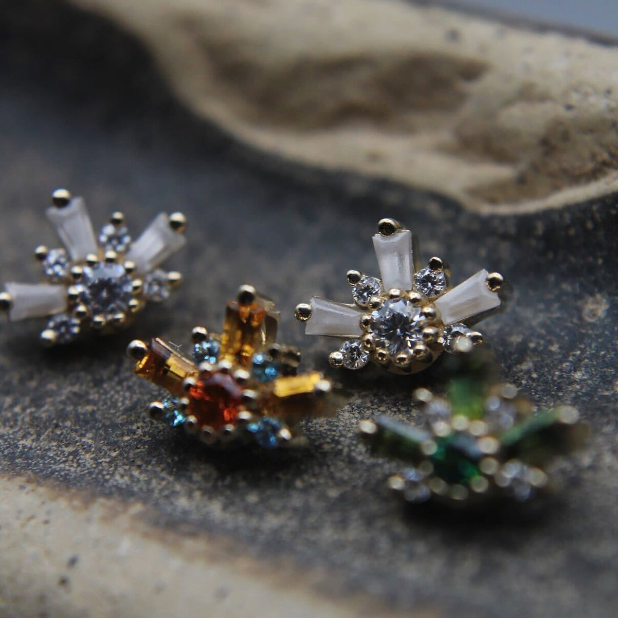 Close-up of decorative earrings on a textured surface featuring orange, green and clear stones