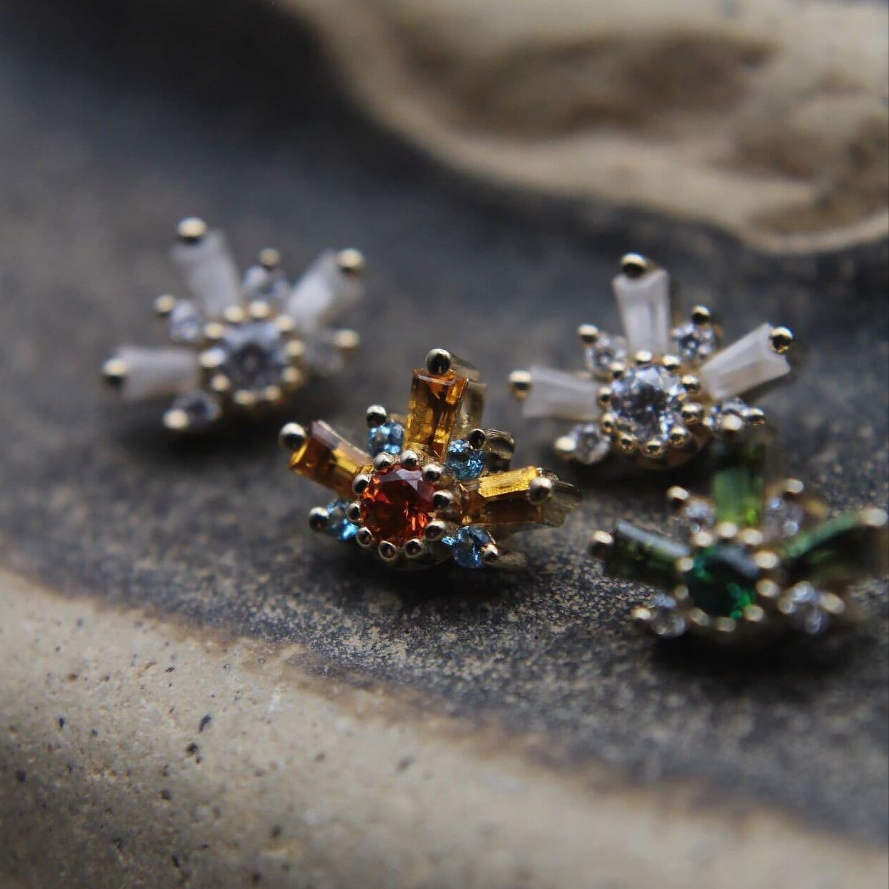 Close-up of decorative earrings on a textured surface featuring orange, green and clear stones