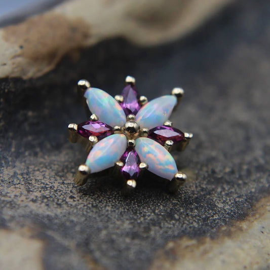 Star-shaped earring with opal and pink gemstones on a textured surface