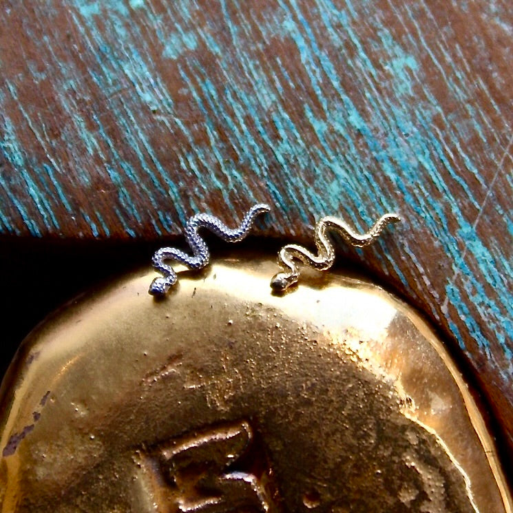 BVLA's "Delicate Snake" shown from left to right in 14k White gold and 14k Yellow gold. Shown on a background featuring a piece of wood with blue paint on top and a golden piece on the bottom of the photo