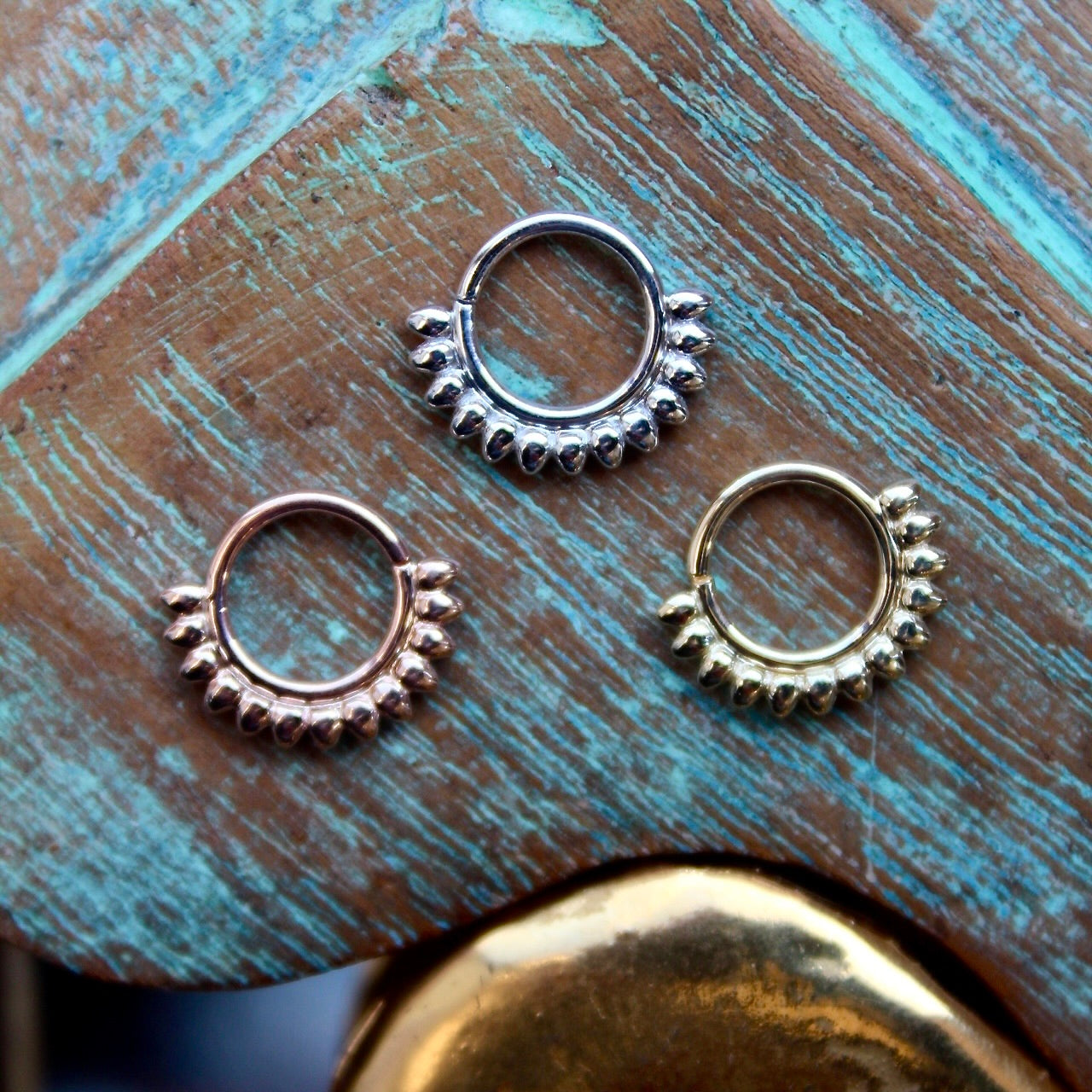 BVLA's "Janus Seam Ring" shown from left to right in 14k Rose gold, 14k White gold and 14k Yellow gold. Shown on a background featuring a piece of wood with blue paint on top and a small golden piece on the bottom of the photo