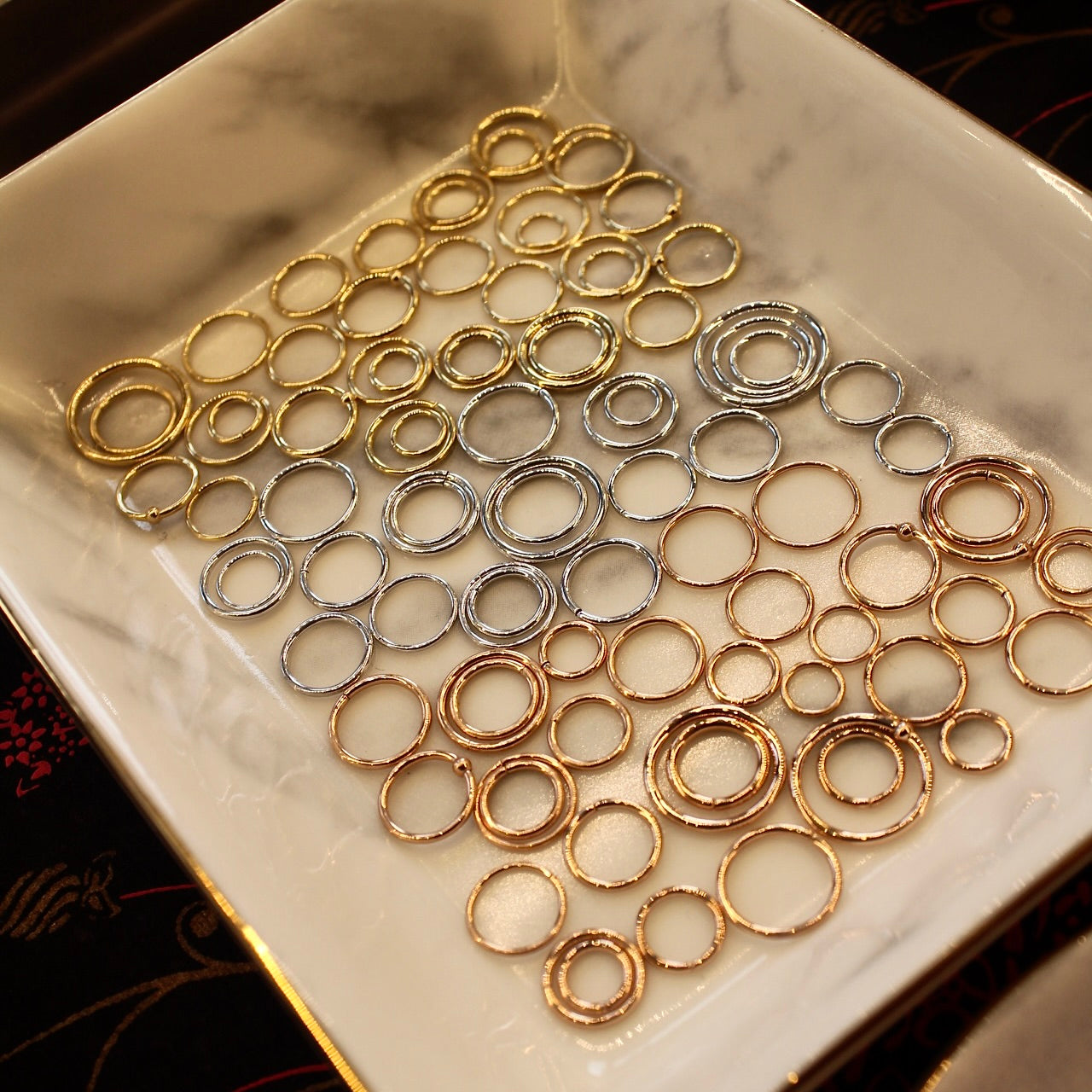 BVLA's "Seam Ring" in groups of 14k Yellow gold, 14k White gold and 14k Rose gold in different sizes. Shown in a square white dish with grey tones throughout and a golded rim.