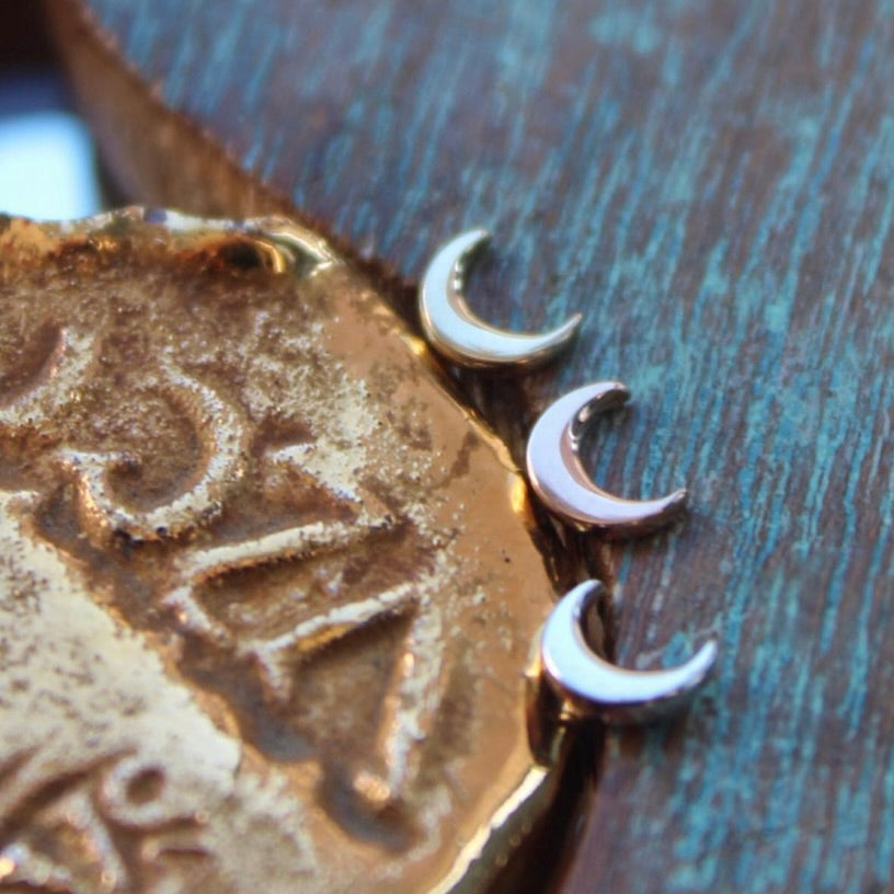 BVLA's "Moon" shown from top to bottom in 14k Yellow gold, 14k Rose gold and 14k White gold. Shown on a background featuring a piece of wood with blue paint on the right and a small golden piece on the left of the photo