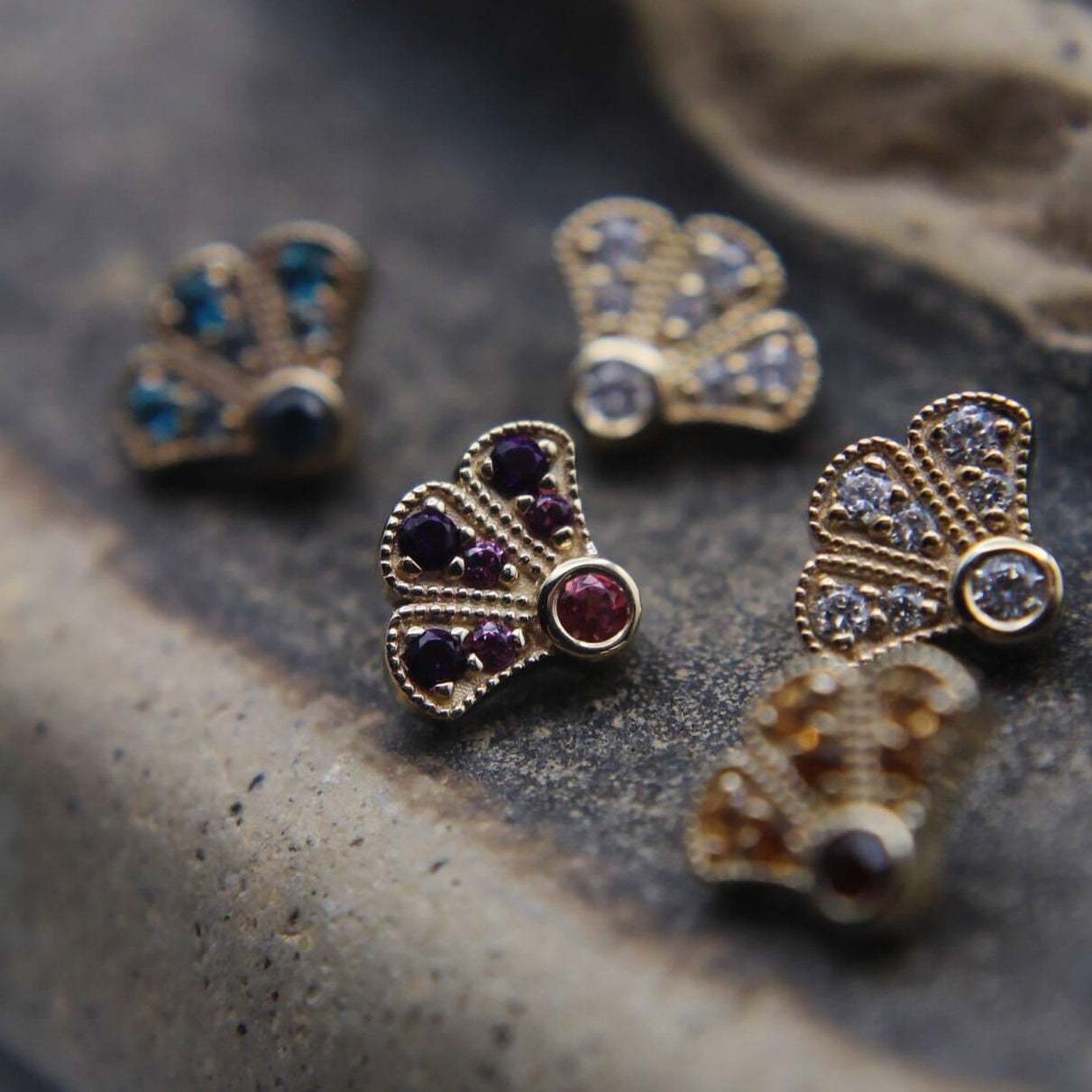 Gold butterfly-shaped earrings with gemstones on a textured stone surface