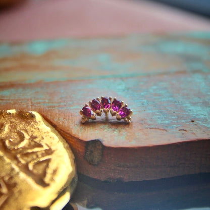 BVLA's "Pear Panaraya" in 14k Yellow gold with 5 Rhodolite Pear cut stones shown on a background featuring a piece of wood with blue paint and a small golden piece on the left side of the photo