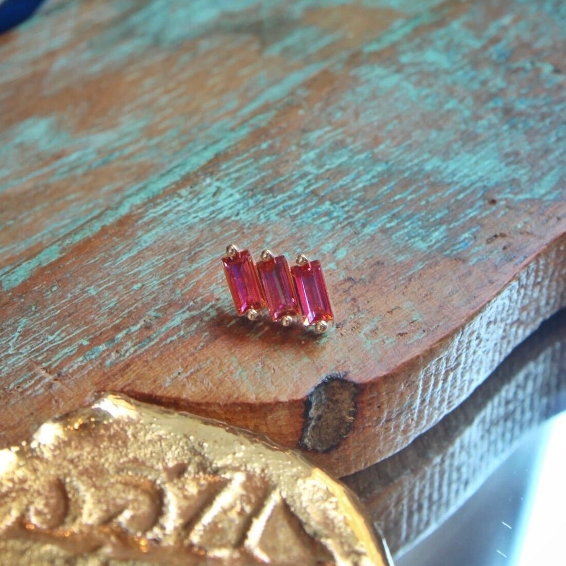 BVLA's "Liara" in 14k Yellow gold with 3 Anastasia Topaz shown on a background featuring a piece of wood with blue paint and a small golden piece on the left side of the photo