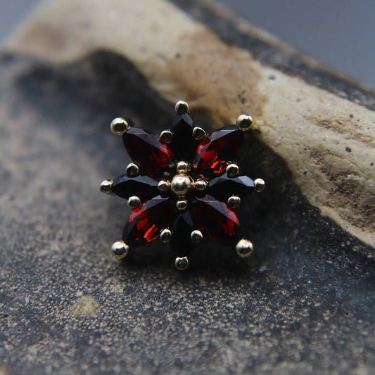 Star-shaped jewelry piece with red and black gemstones and gold accents on a textured surface