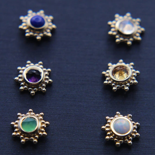 Collection of decorative starburst shaped studs with large gemstone centers on a dark blue background