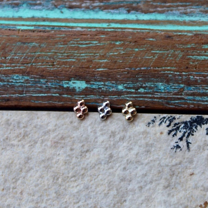 BVLA's "Quad Bead Cluster" shown from left to right in 14k Rose gold, 14k White gold and 14k Yellow gold. shown on a background featuring a piece of wood with blue paint on top and a light grey stone on the bottom of the photo