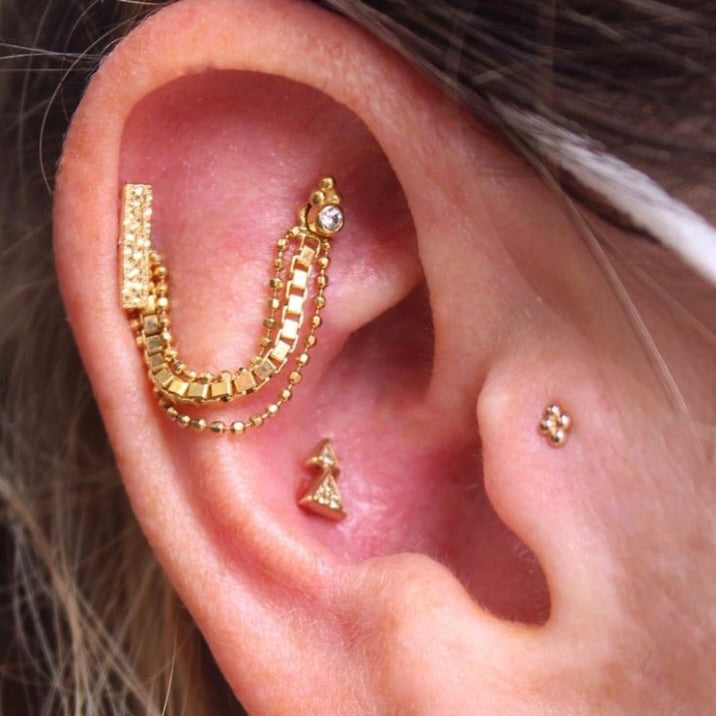 
                  
                    Right ear with BVLA's "Chain" in 14k Yellow gold with 3 links 2 beaded and 1 square links in a draped between 2 healed cartilage piercings. Along with other 14k Yellow gold pieces of jewelry
                  
                