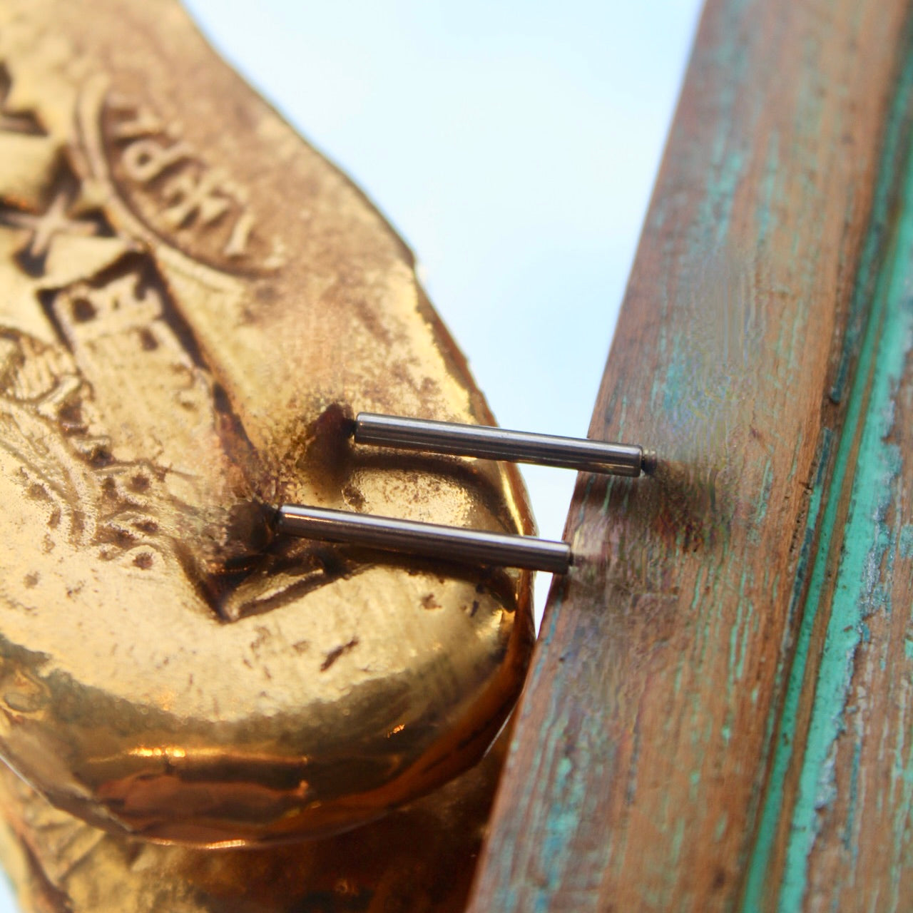 Anatometal's "Straight Barbell" shown in implant grade titanium. Shown on a background featuring a piece of wood with blue paint on the right and a golden piece on the left of the photo